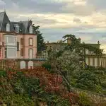 white and brown concrete building surrounded by green trees under white clouds during daytime