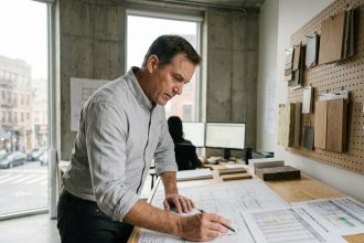 Architecte examinant des plans de construction conformes aux normes RT2012 et RE2020 dans un studio moderne